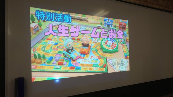 NEXT高等学院の特別活動「人生ゲームとお金」の授業風景。ホワイトボードに掲示されたタイトル。